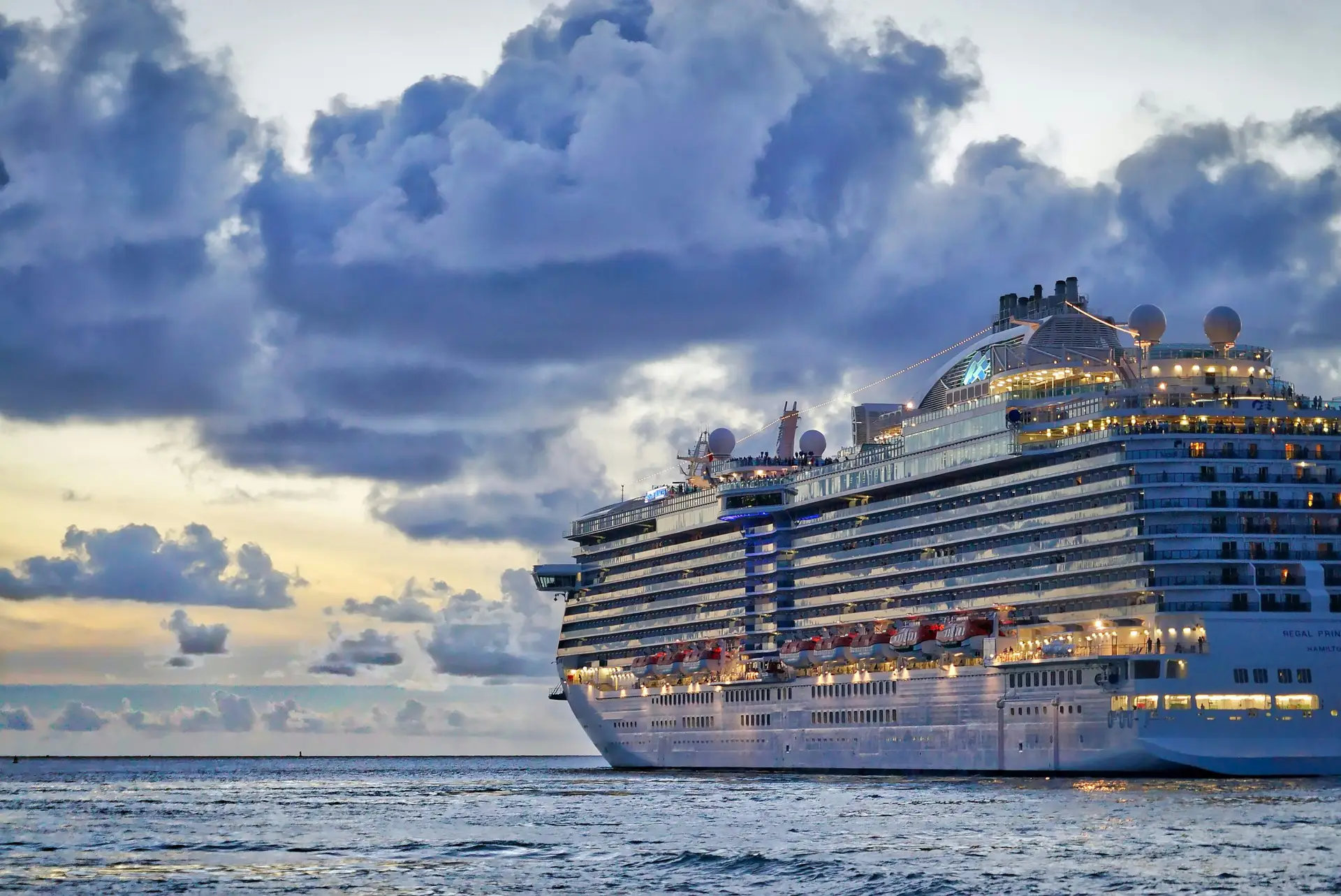 Cruise ship lit up at sea under a dramatic evening sky