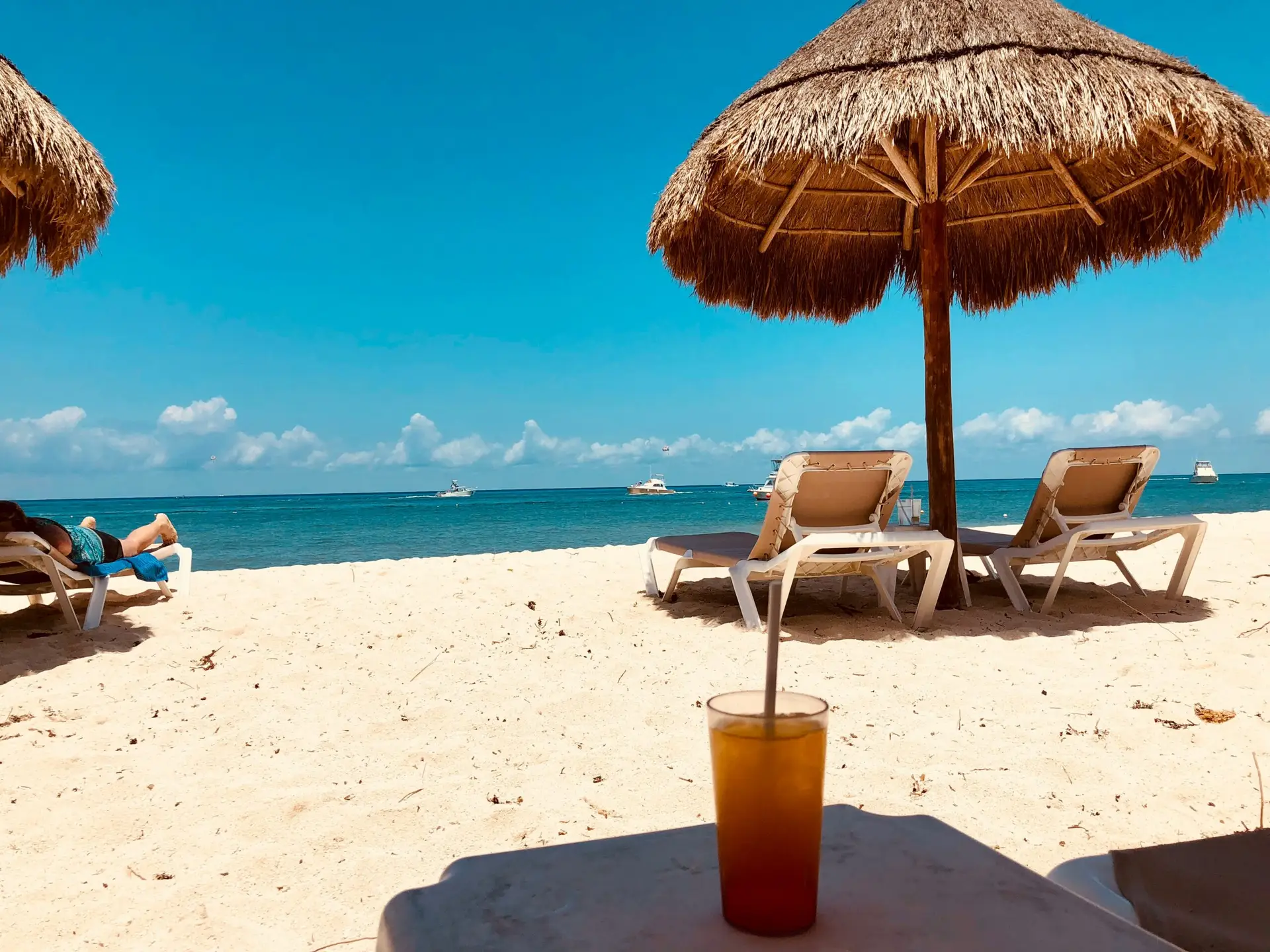 Beach lounge chairs under a thatched umbrella on a turquoise Caribbean shore
